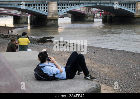LONDON, ENGLAND - September 15, 2019, ein Mann, der im Büro Kleidung liegt auf dem Gehweg am Telefon zu sprechen, der South Bank der Themse Stockfoto