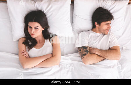 Die jungen Eheleute einander ignorieren im Bett liegend mit gekreuzten Händen Stockfoto