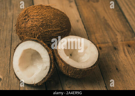 Tropische Kokosnuss Früchte auf einem hölzernen Hintergrund im rustikalen Stil. Eine Mutter ist, die zweite in 2 Teile in der Shell gebrochen ist. Für design Vorlage Stockfoto