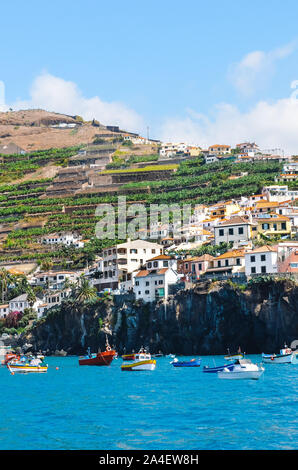 Fischerdorf Camara de Lobos auf Madeira, Portugal fotografiert von den Gewässern des Atlantik. Stadt auf einem Berg an der Küste. Touristische Orte. Bananenplantagen auf dem Hügel. Stockfoto