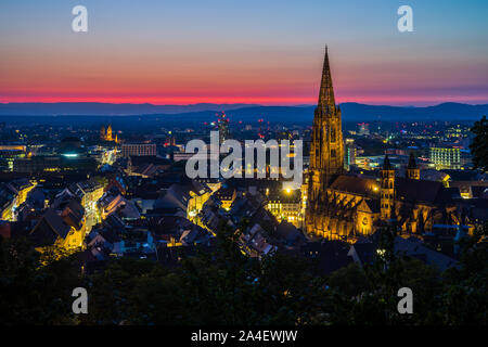 Deutschland, intensive Bunte rote Nachglimmen Himmel verzieren wunderschöne Skyline der mittelalterlichen Stadt Freiburg im Breisgau mit beleuchteten Gebäuden und Straßen Stockfoto