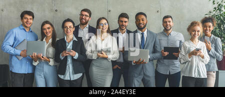 Junge Geschäftsleute mit verschiedene Geräte im Büro posing Stockfoto