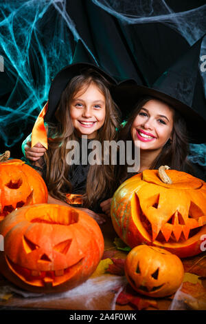 Nahaufnahme wunderschöne kaukasische Mutter und ihre Tochter in Hexenkostümen Feiern Halloween posiert mit gekrümmten Kürbissen Stockfoto