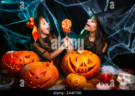 Mutter und ihrer Tochter in Hexe Kostüme Halloween Feiern mit Halloween Süßigkeiten und süße über Spider web Stockfoto