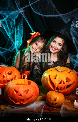 Nahaufnahme wunderschöne kaukasische Mutter und ihre Tochter in Hexenkostümen Feiern Halloween posiert mit gekrümmten Kürbissen Stockfoto