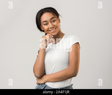 Smiling Girl posiert und berührend Kinn über grauer Hintergrund Stockfoto