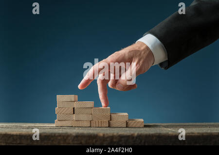 Geschäftsmann seinen Finger nach oben, um die Treppen aus Holz in einem konzeptionellen Bild. Über Marine blauen Hintergrund. Stockfoto