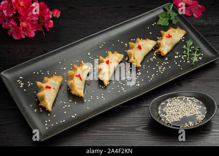 Ebi gedza Chinesische gebratene Knödel mit Garnelen und Gemüse in einer schwarzen Platte auf einem dunklen Hintergrund, serviert mit Sauce Stockfoto