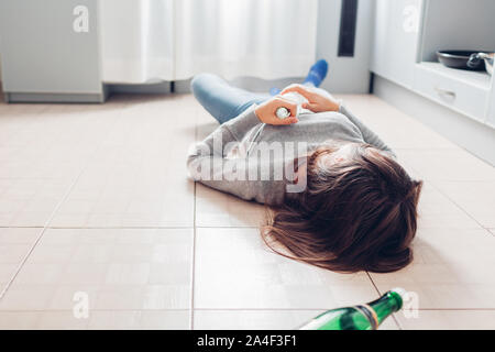 Weibliche Alkoholabhängigkeit. Junge Frau schlafen auf Küche Etage nach, die Flasche Stockfoto