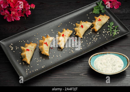 Ebi gedza Chinesische gebratene Knödel mit Garnelen und Gemüse in einer schwarzen Platte auf einem dunklen Hintergrund, serviert mit Sauce Stockfoto
