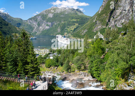 Touristen entlang einem Gehweg neben dem Geiranger Wasserfall und die großen Kreuzfahrtschiffe auf Geiranger Fjord, Vestlandet, Norwegen Stockfoto