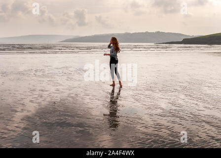 Junge rothaarige Frau zu Fuß am Sandstrand hinterlassen Spuren im Sand. Bewölkten Tag. Stockfoto