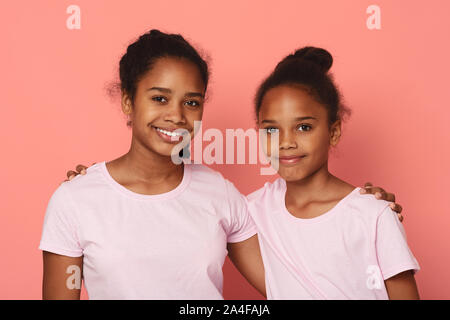 Portrait von niedlichen kleinen Schwestern umfassend über rosa Hintergrund Stockfoto