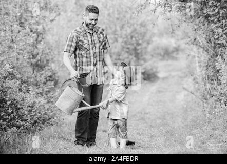 Eco Farm. mit Gießkanne und Topf. Gartengeräte. kleiner Junge Kind helfen Vater in der Landwirtschaft. Vater und Sohn in Cowboy Hut auf Ranch. happy Earth Day. Stammbaum nursering. Am besten in unserer Sphäre. Stockfoto