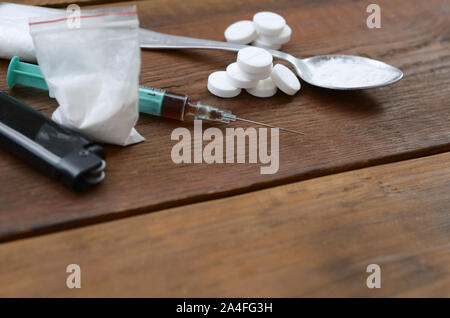 Eine Menge von Betäubungsmitteln und Geräte für die Zubereitung von Drogen liegen auf einem alten Holztisch. Drogendealer Material. Heroin und Methamphetamin im raw Stockfoto