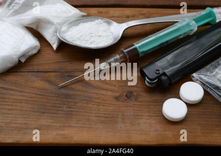 Eine Menge von Betäubungsmitteln und Geräte für die Zubereitung von Drogen liegen auf einem alten Holztisch. Drogendealer Material. Heroin und Methamphetamin im raw Stockfoto