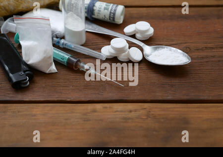 Eine Menge von Betäubungsmitteln und Geräte für die Zubereitung von Drogen liegen auf einem alten Holztisch. Drogendealer Material. Heroin und Methamphetamin im raw Stockfoto