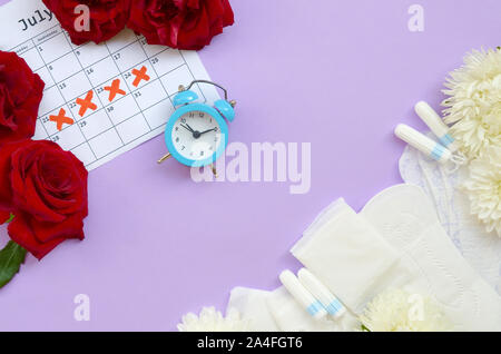 Menstruationszyklus Pads und Tampons auf Menstruation Periode Kalender Wecker mit blauen und roten Rosen. Aspekte der Frauen Wellness in Monatszeitschriften. Frau c Stockfoto