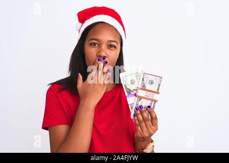 Junge afrikanische amerikanische Frau Mütze tragen und halten Bündel von Dollar Banknoten Mund bedecken mit Hand mit Schande für Fehler schockiert, Expres Stockfoto