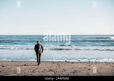 Tween Junge trägt einen Neoprenanzug zu Fuß in die Brandung am Strand Stockfoto