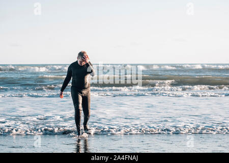 Tween Junge in einem Neoprenanzug zu Fuß am Strand Land nach unten schauen. Stockfoto