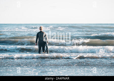 Tween Junge trägt einen Neoprenanzug und halten ein Surfbrett am Strand Stockfoto