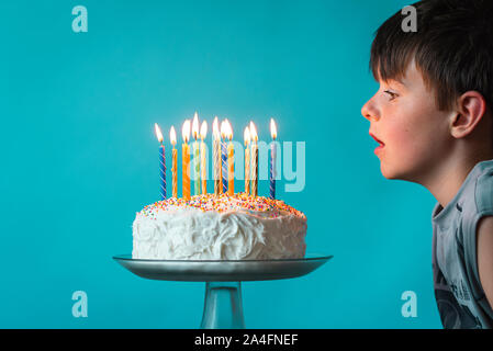 Junge bereit, Kerzen auf der Geburtstagstorte vor blauem Hintergrund Blasen. Stockfoto