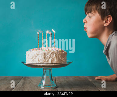 Junge ausblasen Kerzen auf der Geburtstagstorte vor blauem Hintergrund. Stockfoto