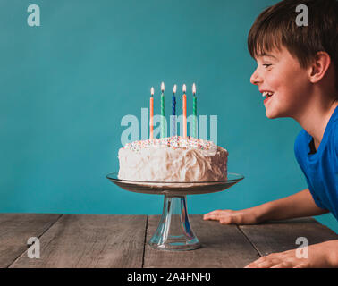 Junge bereit, Kerzen auf der Geburtstagstorte auf blauem Hintergrund Blasen. Stockfoto