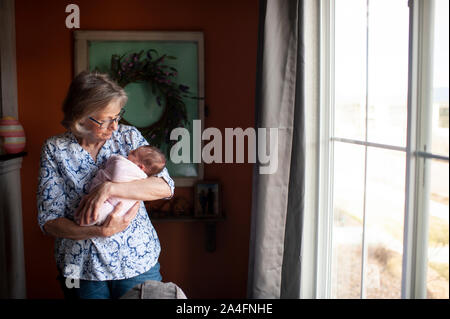 Großmutter Holding neugeborene Enkelin durch Fenster zu Hause Stockfoto