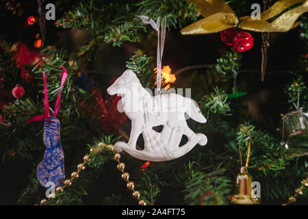 Weihnachten Spielzeug in Form einer weißen Keramik antik Schaukelpferd mit Geschenken auf einem geschmückten Weihnachtsbaum. Close-up. Stockfoto