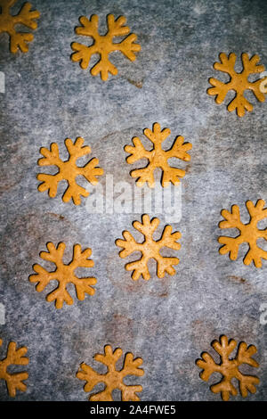 Lebkuchen cookie Schnitt in Form einer Schneeflocke vom rohen Teig auf Pergament Backpapier auf einem dunklen Hintergrund. Blick von oben. Platz sparen Stockfoto