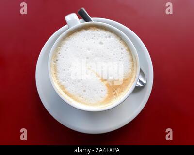 Cappuccino Tasse roten Hintergrund. Tasse Kaffee mit silbernen Löffel. Cappuccino Draufsicht mit dem Raum. Stockfoto