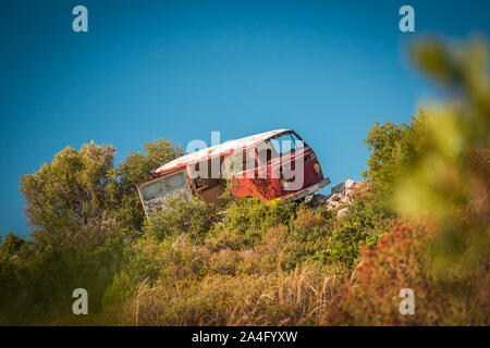 Abgebrochene van Bus auf den Felsen in der Mitte von Nirgendwo an einem sonnigen Tag. Unscharf Bäume im Vordergrund, Schuß aus der Entfernung. Stockfoto