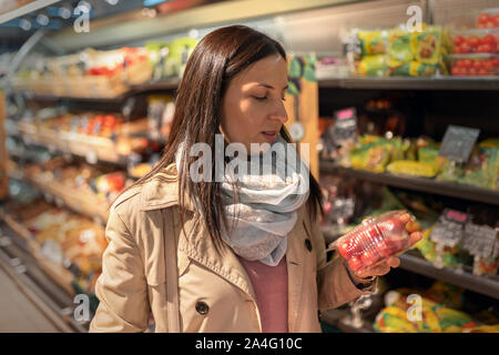 Hausfrauen, Frauen mit Warenkorb im Supermarkt. Wunderschöne junge Frau mit einem Warenkorb Blick auf einige Produkte auf einen Supermarkt in Gang. Frau Stockfoto