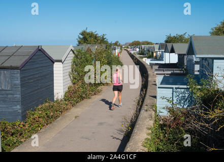 Jogger laufen am Meer entlang der Wand zwischen dem Strand Hütten in Whitstable, Kent Stockfoto