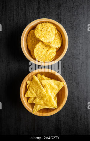 Runde, dreieckige Nacho Chips. Gelbe Tortilla Chips in der Schüssel auf Schwarz. Ansicht von oben. Stockfoto