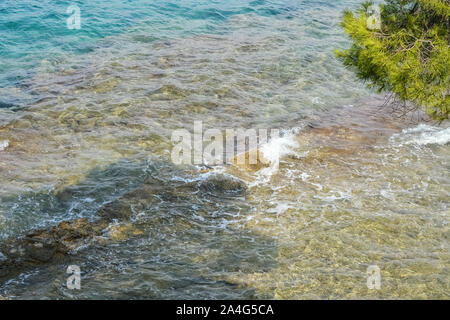 Kleine Wellen an der Küste Teil der Roten Insel in Kroatien aus einem felsigen Ufer. Ein felsiger Boden sichtbar ist durch die transparente Oberfläche des Wassers. Stockfoto