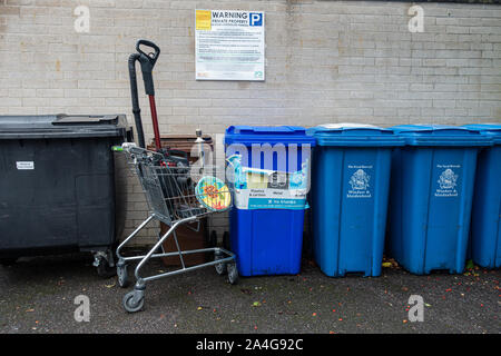 Wheelie Bins und einem verlassenen Supermarkt Trolley mit Müll mit einer Mauer mit einem Schild über parken. Stockfoto