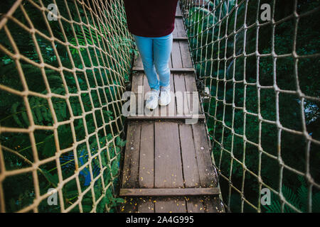 Den unteren Abschnitt des ein Mädchen steht auf einer Swinging Bridge im Regenwald