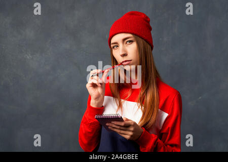 Mädchen hält Notizblock, Stift auf texturierte Wand isoliert Stockfoto