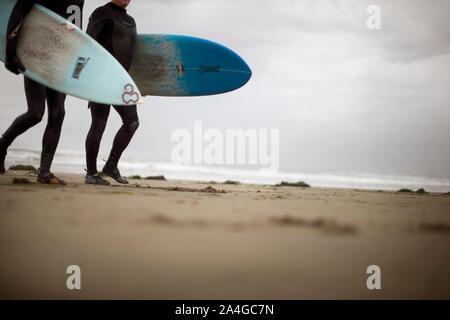 Zwei Männer Anzüge tragen und Surfboards beim Gehen entlang einem Sandstrand. Stockfoto