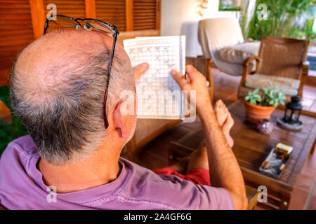 Pensionierter Mann verbringt seine Zeit mit der Lösung von langweiligen Kreuzworträtsel auf der Veranda seines Hauses. Stockfoto