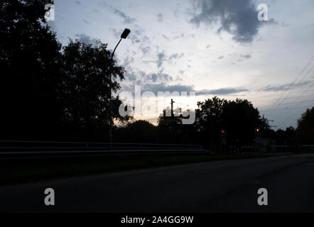 Blick auf einen Zug an einem Bahnübergang mit wartenden Person unter einem Himmel im Bezirk Emsland im Nordwesten von Deutschland Stockfoto