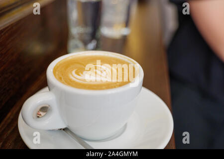 Close Up und Top Aussicht auf schöne latte Kunst mit Herz Muster auf der Oberseite des Kaffee Cappuccino aus weisser Keramik Schale auf Holz Zähler in Coffee Bar. Stockfoto
