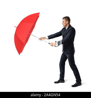 Ein junger Geschäftsmann steht auf weißem Hintergrund und Häute von rauen Umgebung hinter einem offenen roten Regenschirm. Stockfoto