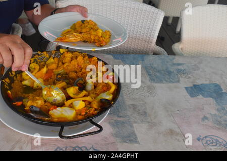 Meeresfrüchte Paella aufgetischt auf dem Tisch in einem Restaurant am Meer. Risotto, Garnelen, Muscheln, Muscheln, Tintenfisch, Fisch und Paprika in eine traditionelle Paella pot. Stockfoto