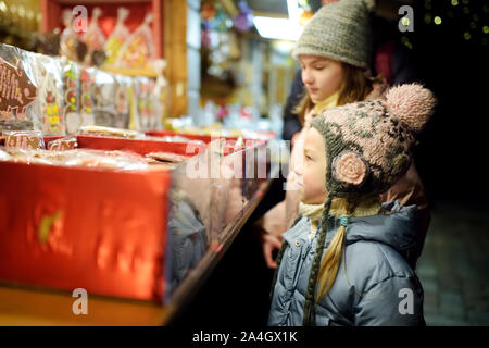 Nette junge Schwestern Spezialitäten Auswahl auf den traditionellen Weihnachtsmarkt in Riga, Lettland. Kinder kaufen Candy und Cookies auf Weihnachten. Happy Family Zeit an kühlen Stockfoto