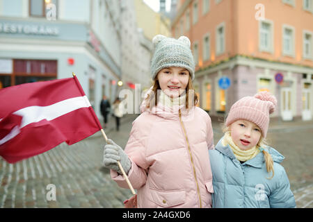 Zwei Entzückende kleine Schwestern feiern Lettischen Unabhängigkeitstag holding Lettland Flagge in Riga, Lettland Stockfoto