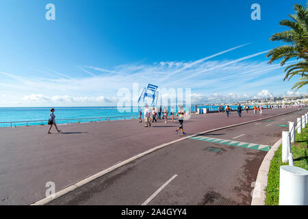 Jogger und Walker Pass durch die blauen Stuhl Auslastungsverteilung entlang der Promenade des Anglais an der französischen Riviera in Nizza Frankreich entlang dem Mittelmeer. Stockfoto